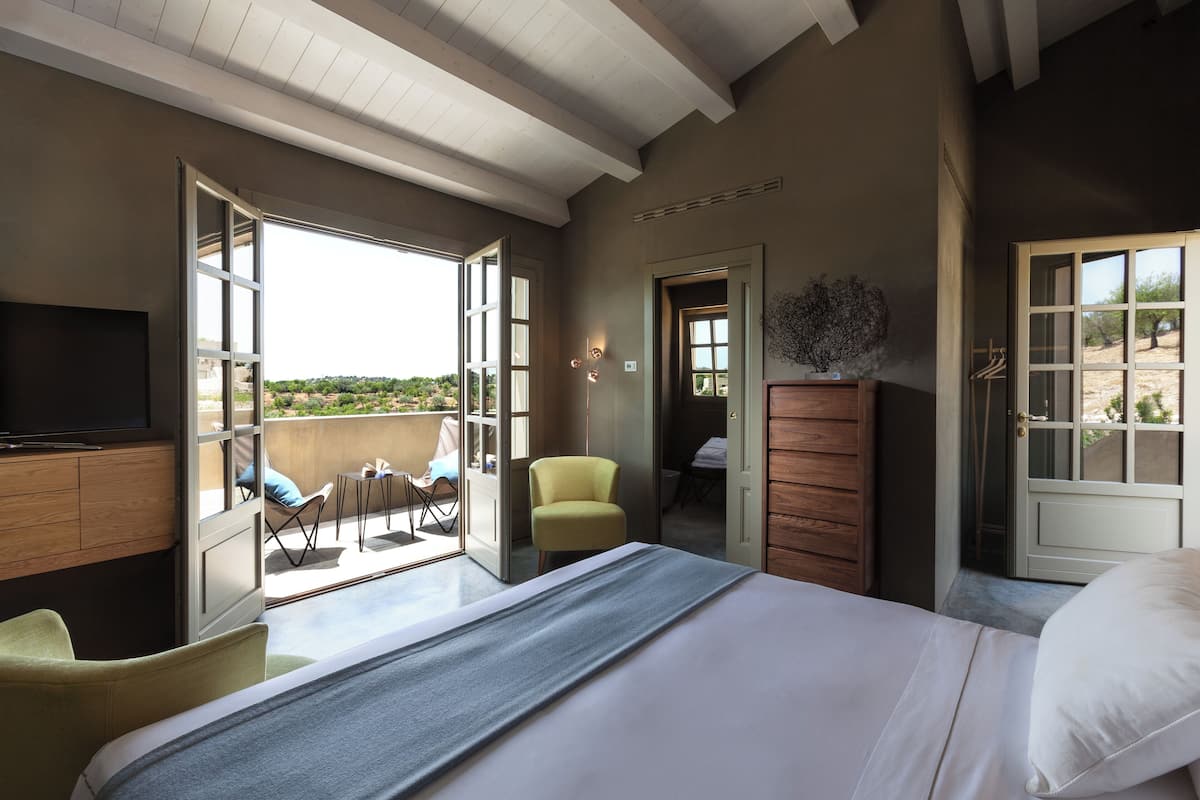 A bedroom with a bed, a television, a chair, a desk, and a view of the outdoors.