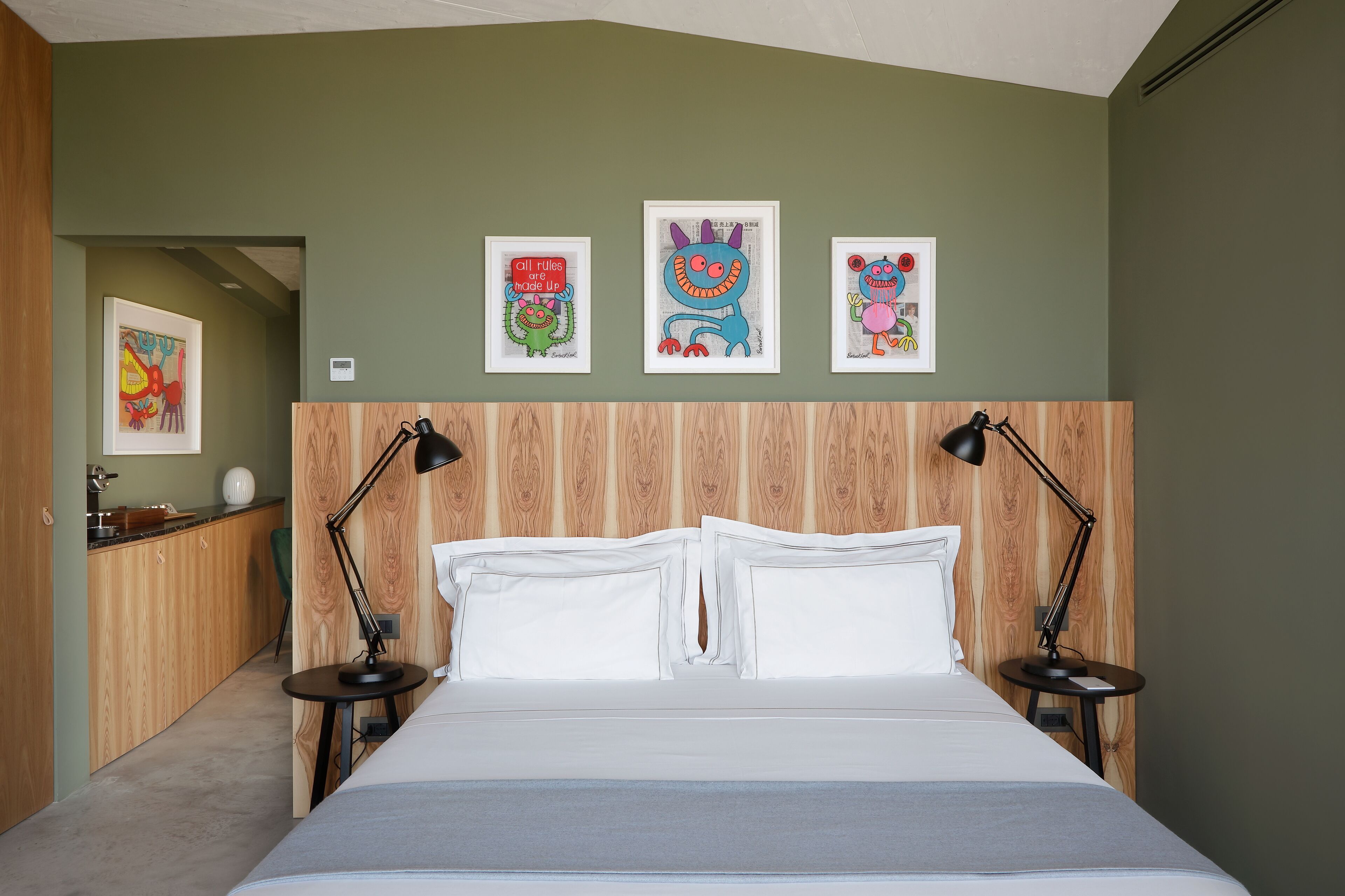 Une chambre à coucher avec une tête de lit en bois, du linge de lit blanc et trois œuvres d’art encadrées accrochées au mur.