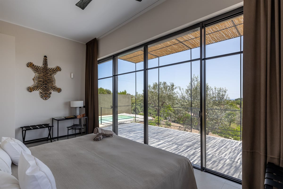 A modern hotel room with a large bed, a desk, and a view of a pool and trees.