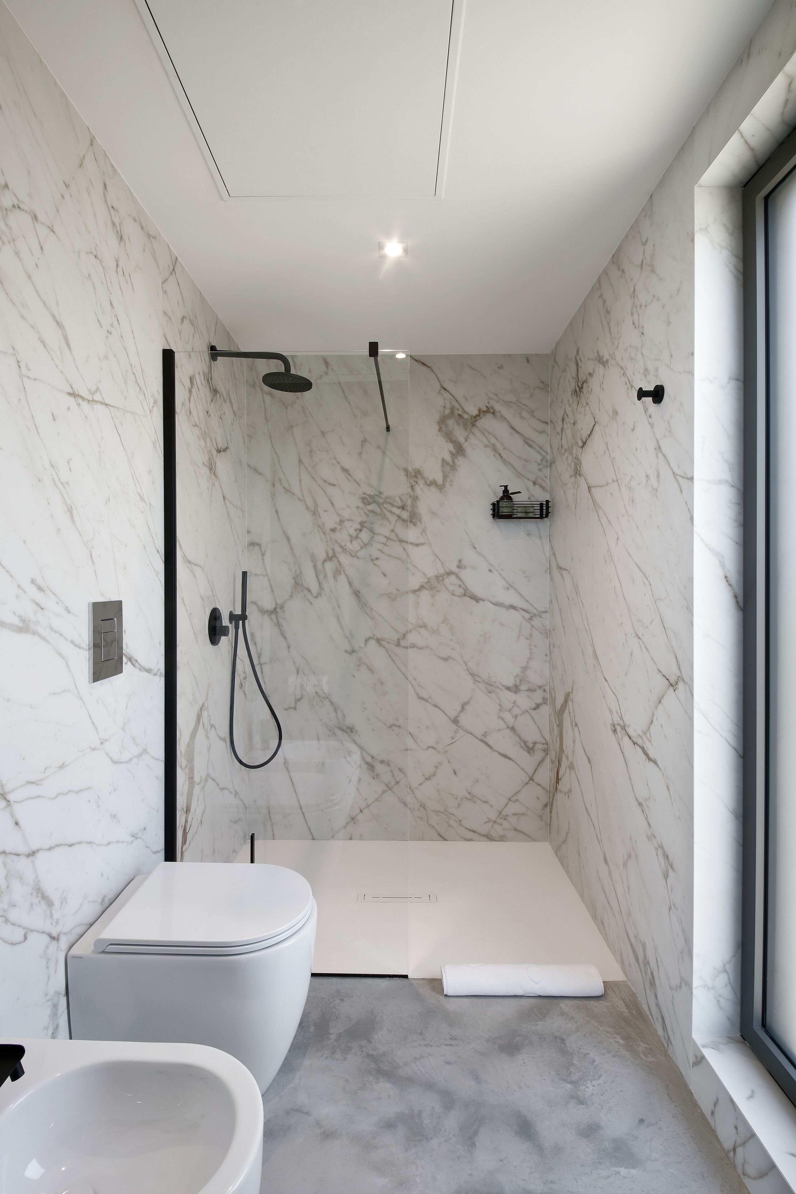 A modern bathroom with a bathtub, shower, and toilet, all against marble walls.