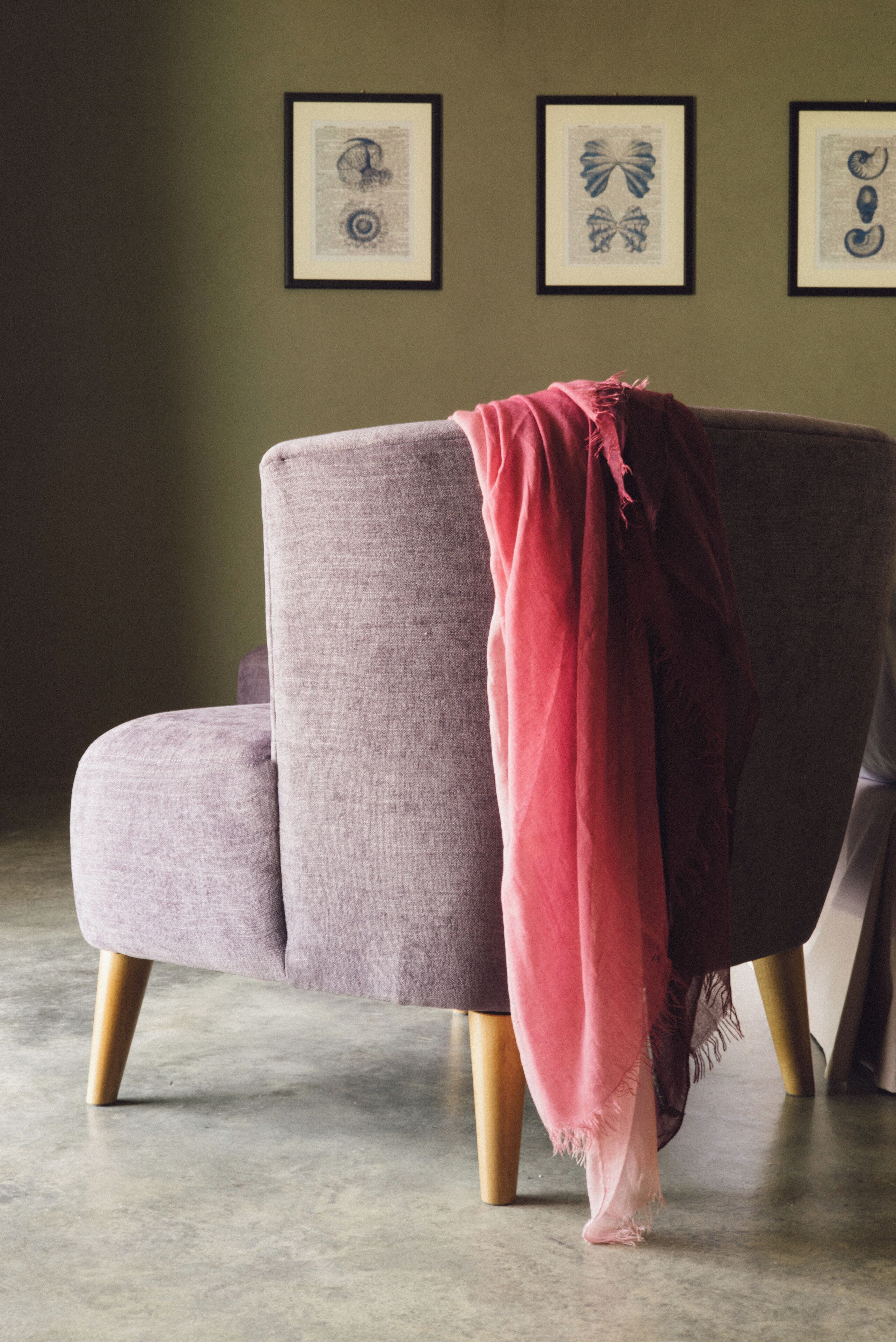 Una habitación con un sillón gris, una manta roja y cuadros en la pared.