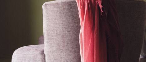 Una habitación con un sillón gris, una manta roja y cuadros en la pared.