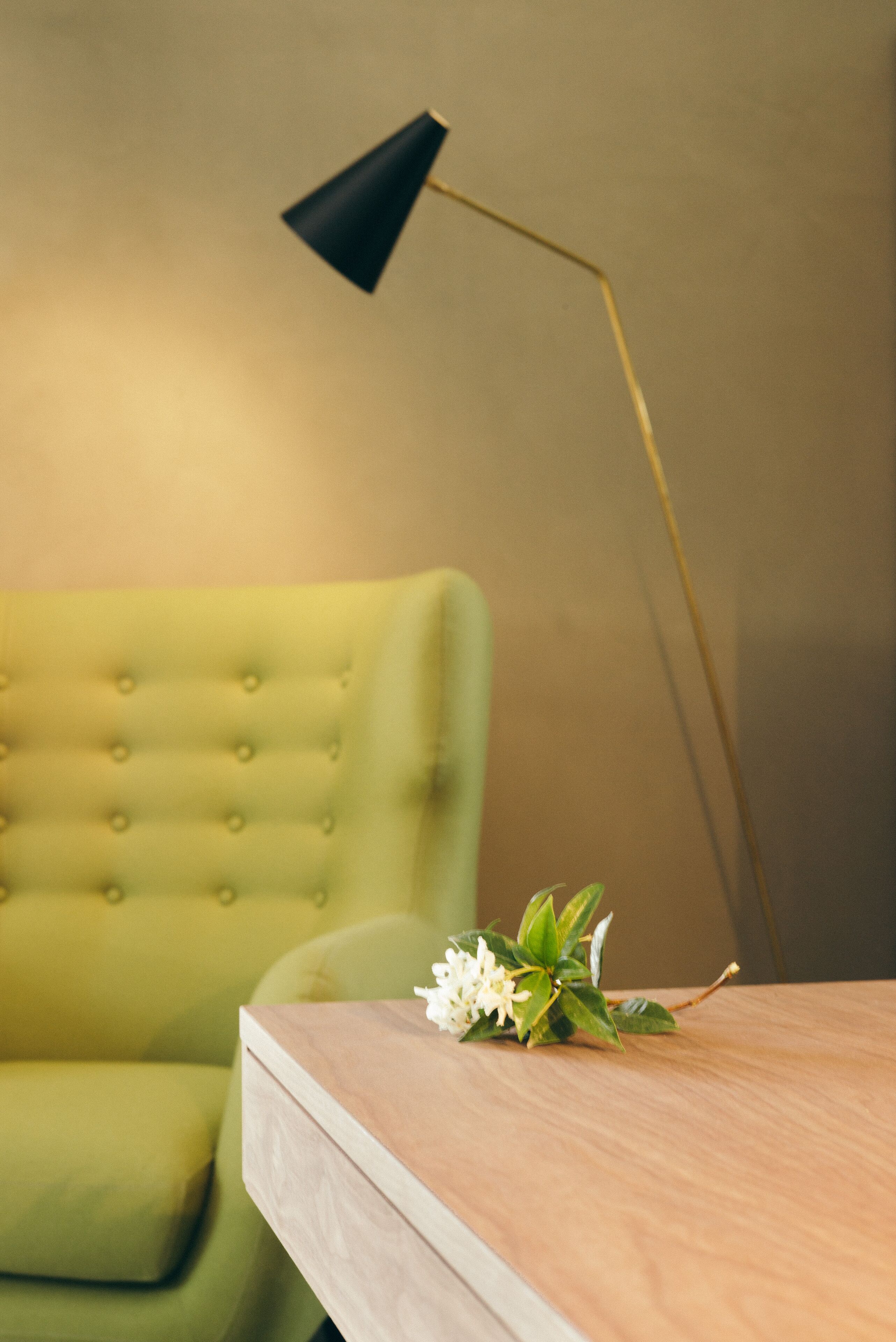 A green armchair and a wooden table with a black lamp and a flower arrangement.