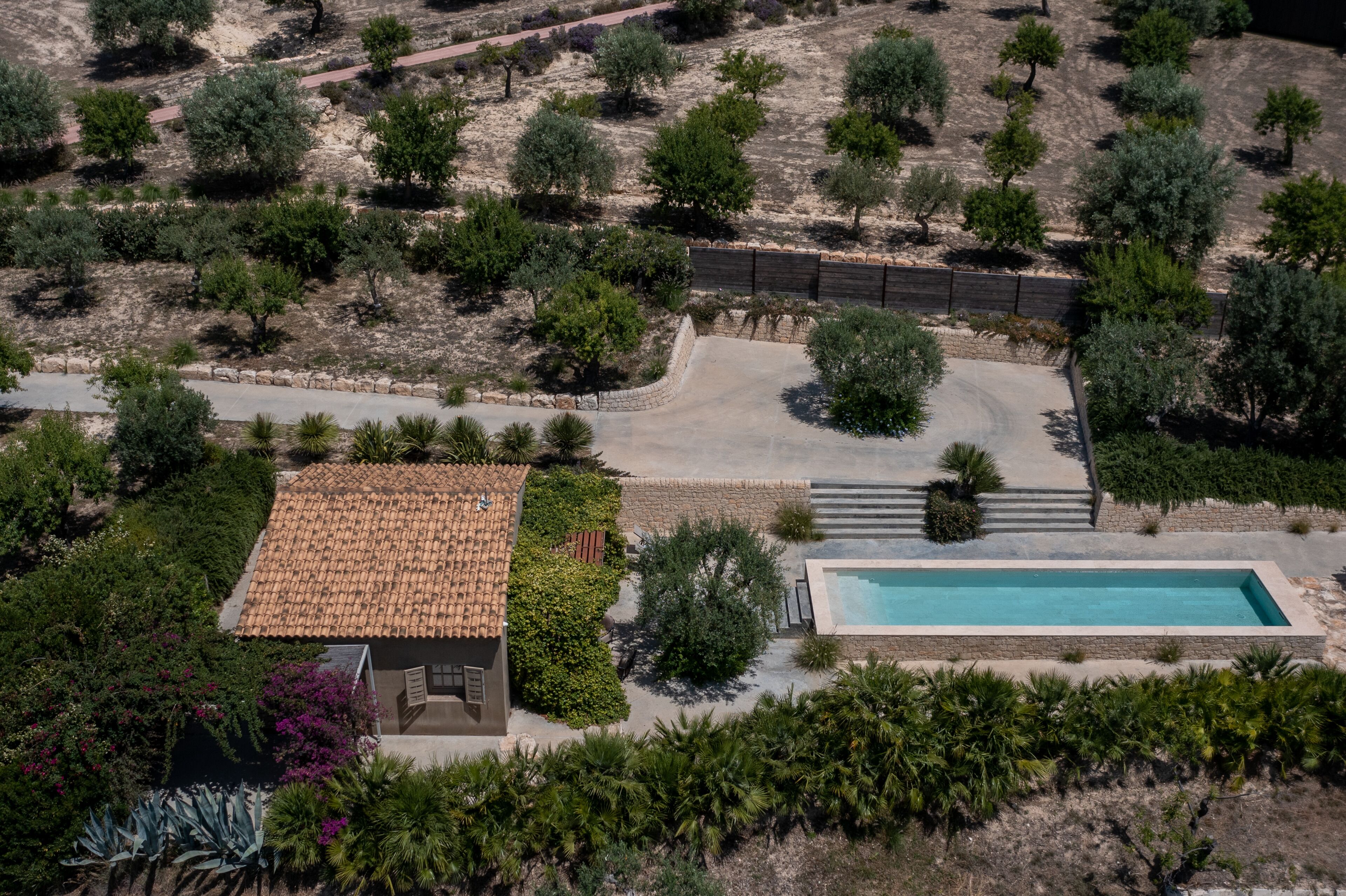 Vista aérea de uma propriedade com piscina, área de pátio e jardim com diversas árvores e arbustos.
