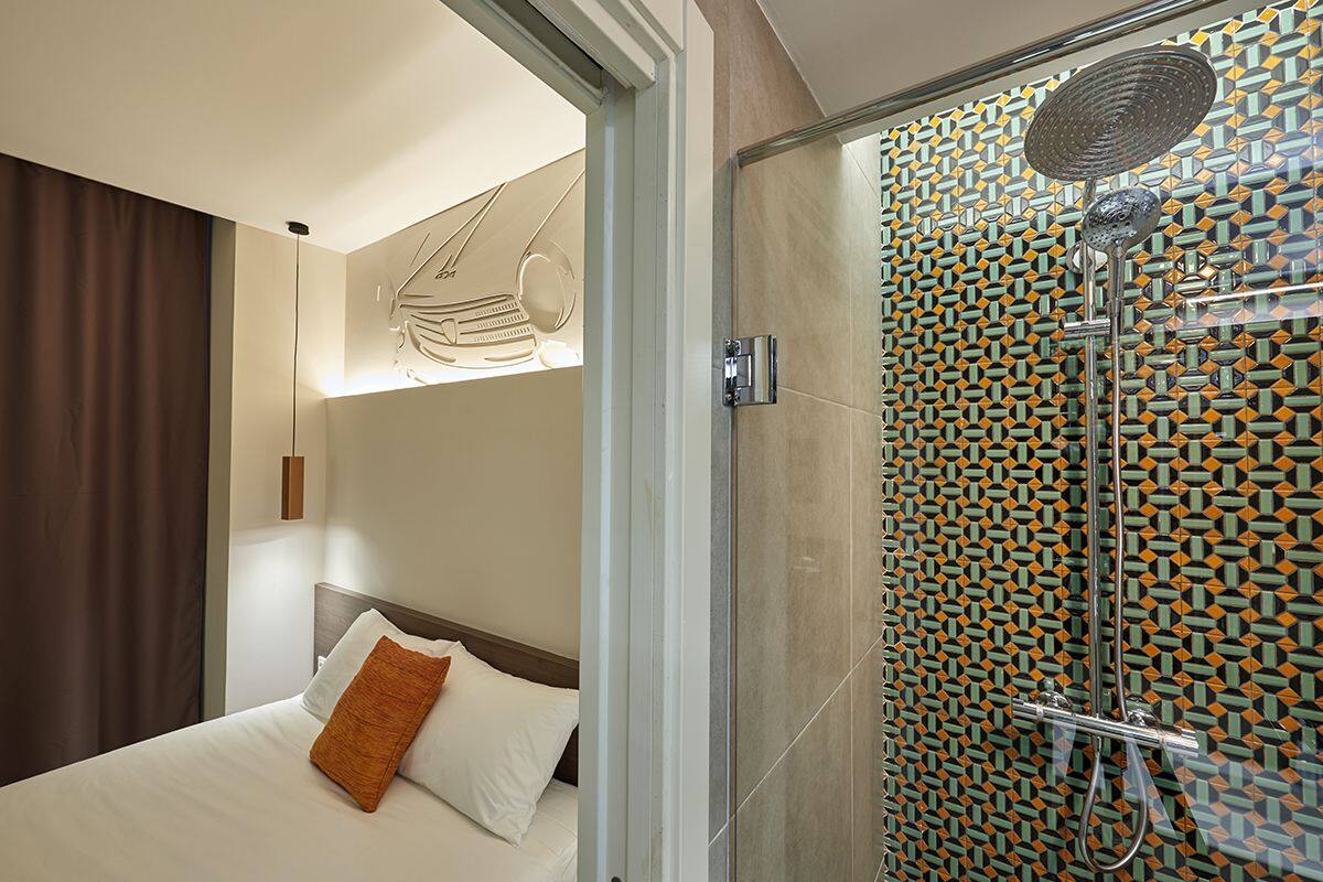 Une chambre d’hôtel moderne avec un lit, une douche dont le mur est recouvert de carreaux décoratifs, et un luminaire au plafond.