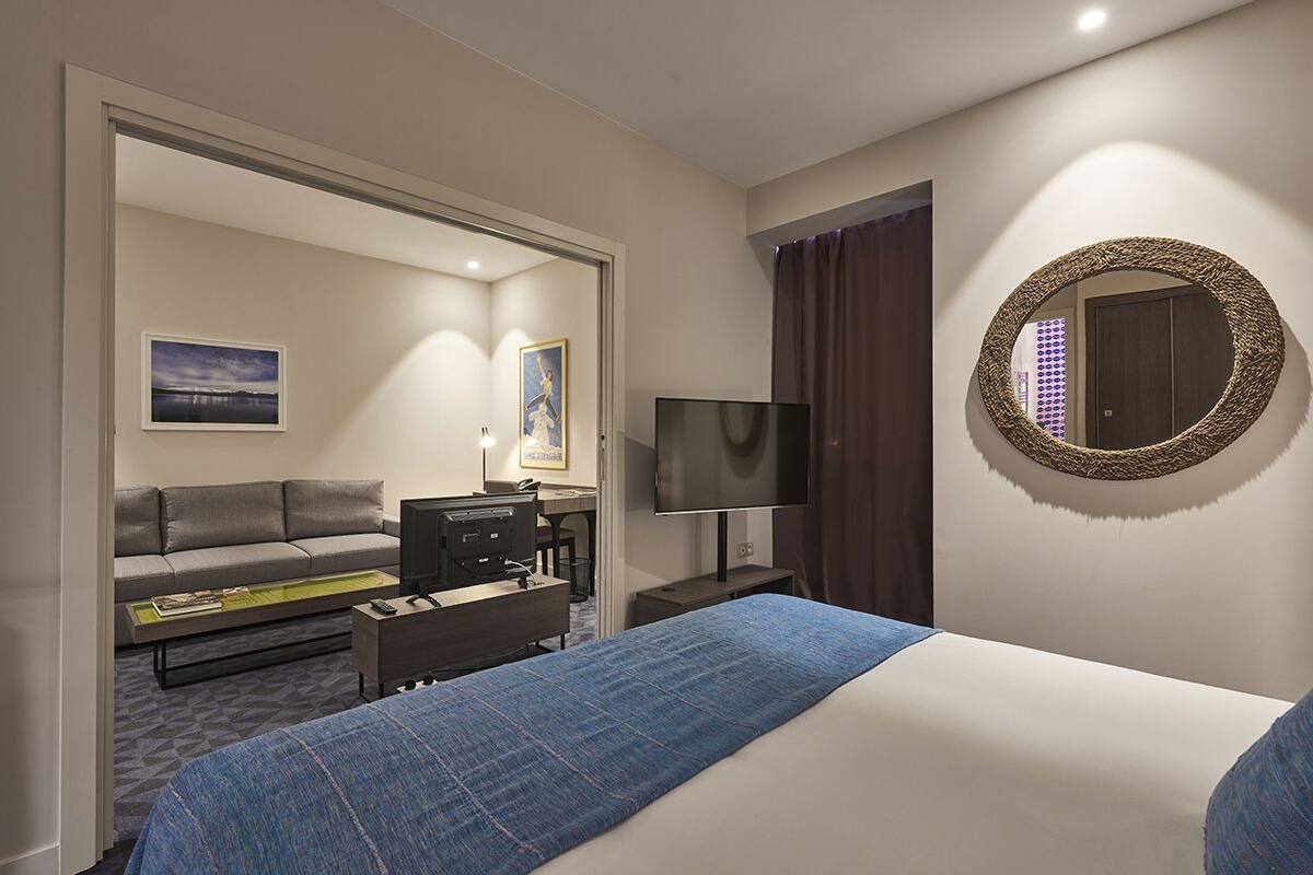Une chambre d’hôtel comprenant un lit, un canapé, un bureau avec un ordinateur, une télévision et un miroir.