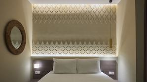 A neatly made bed with a headboard featuring a geometric pattern, a round mirror on the wall, and two bedside tables. - M Suite Hotel (Algiers)