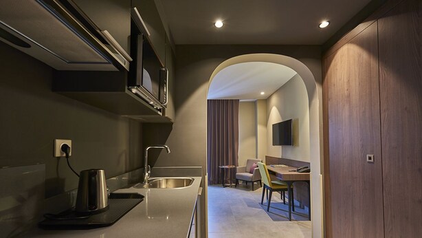A modern kitchen with a built-in stove, a microwave, and a sink. There is a dining area with a table and chairs visible through an archway. - M Suite Hotel (Algiers)