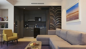 A modern living room with a sofa, a coffee table with a magazine, a yellow armchair, and a kitchen in the background. - M Suite Hotel (Algiers)