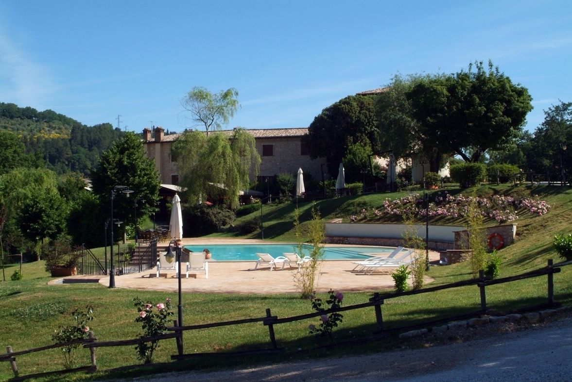 Un espace piscine avec des chaises longues, une pergola et un bâtiment en pierre en arrière-plan.