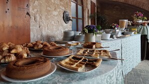 Buffet de l'esmorzar amb pastissos, pastissos i una zona de cafè en un ambient rústic amb parets de pedra i una porta de fusta.