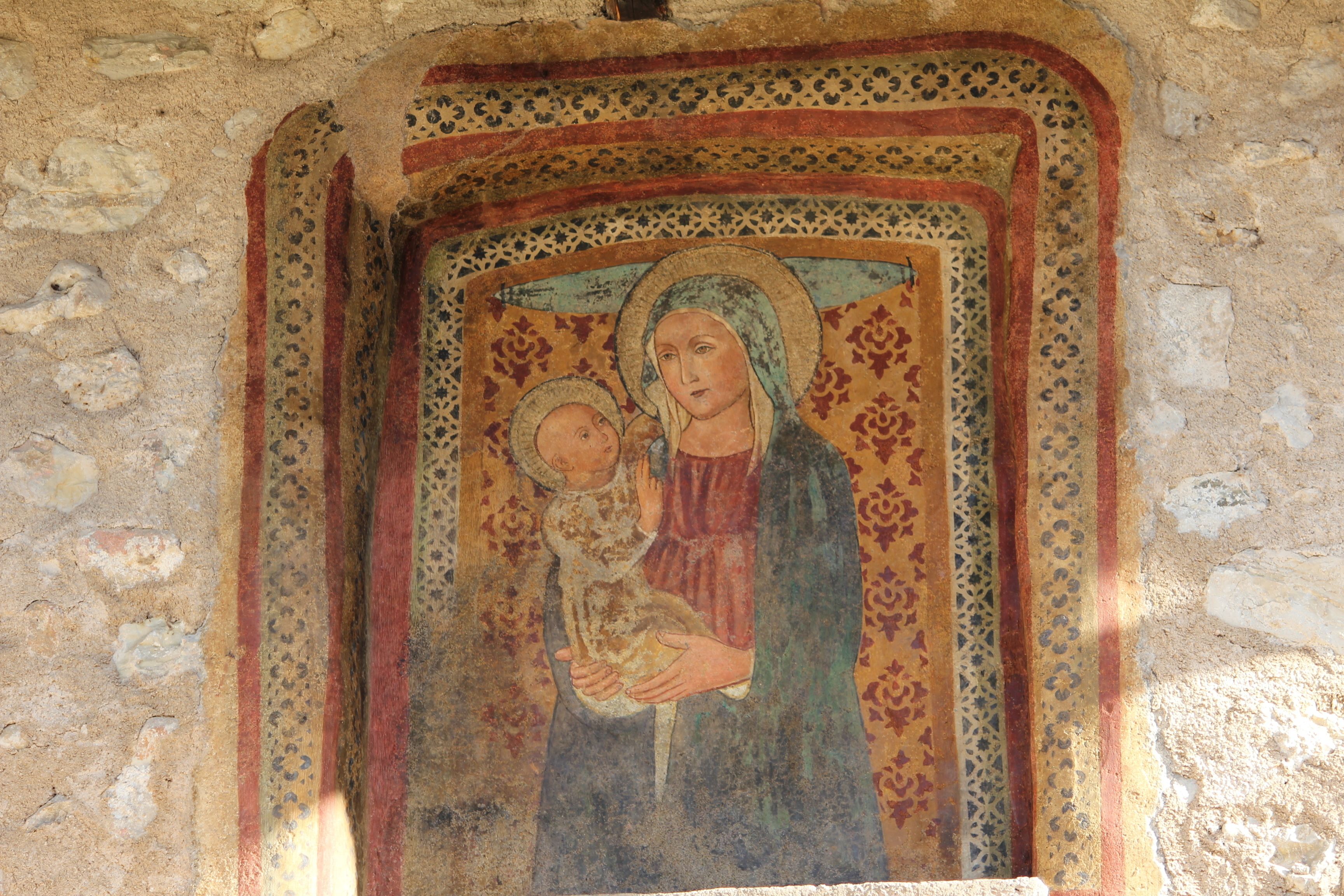 A fresco with a religious figure holding a child, framed by ornate patterns.