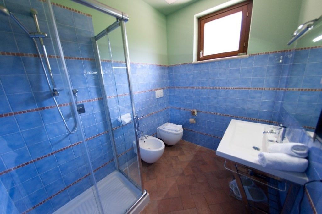 Un baño con azulejos azules, cerramiento de ducha de vidrio, lavamanos blanco y un bidé.