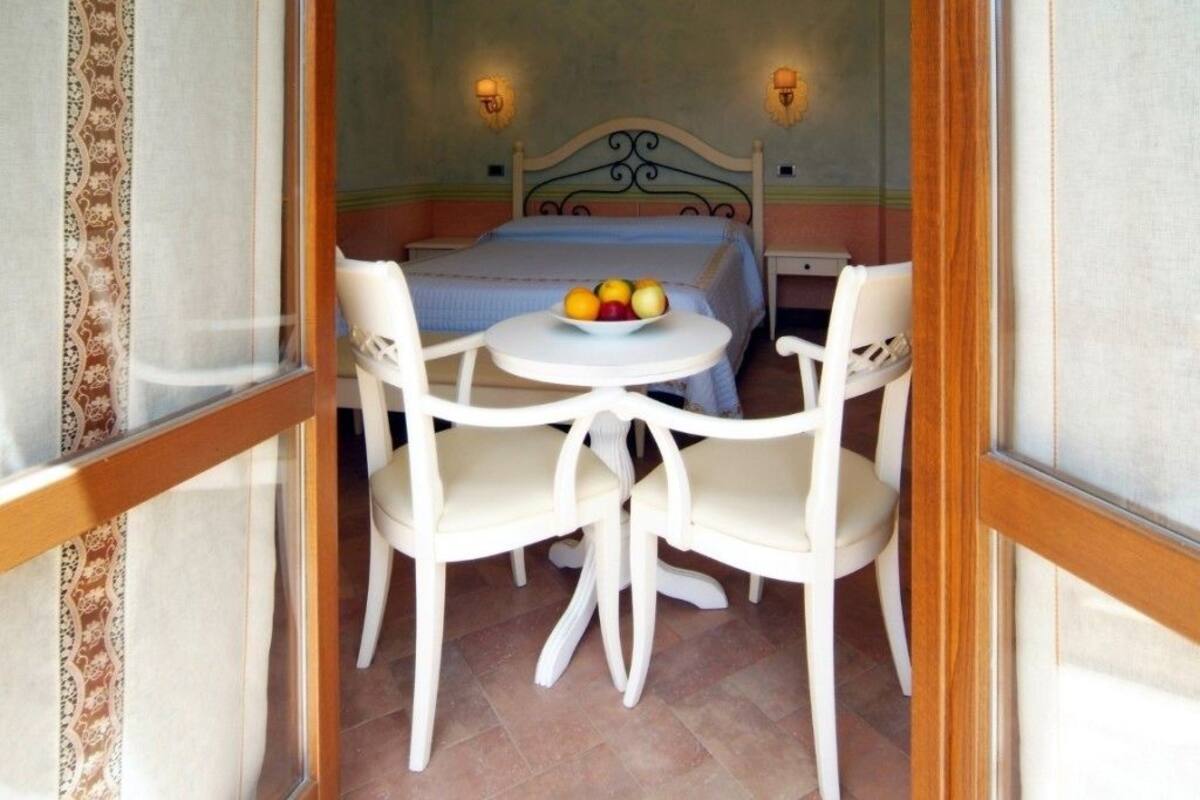 A room with a bed, a round table with chairs, and a fruit bowl on the table.