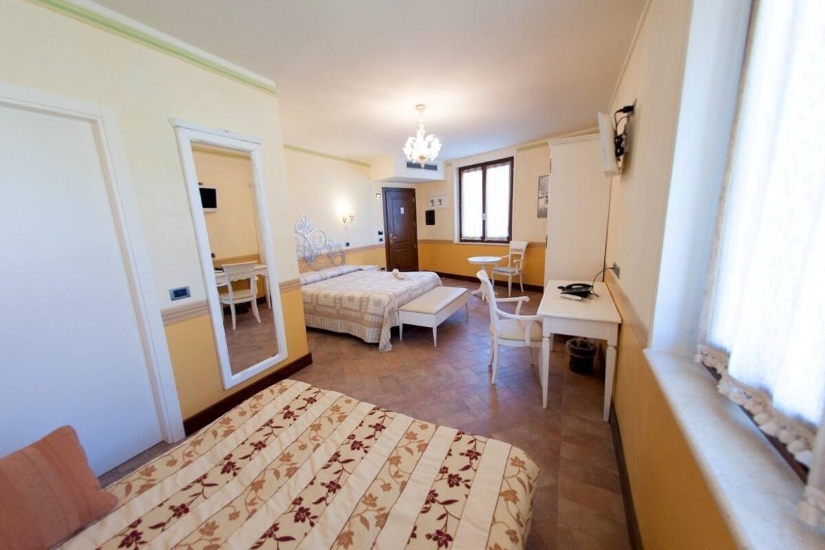 A bedroom with a bed, a desk, a chair, a mirror, and a window.