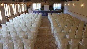 A large hall with rows of white chairs, a stage with a table, and large windows.