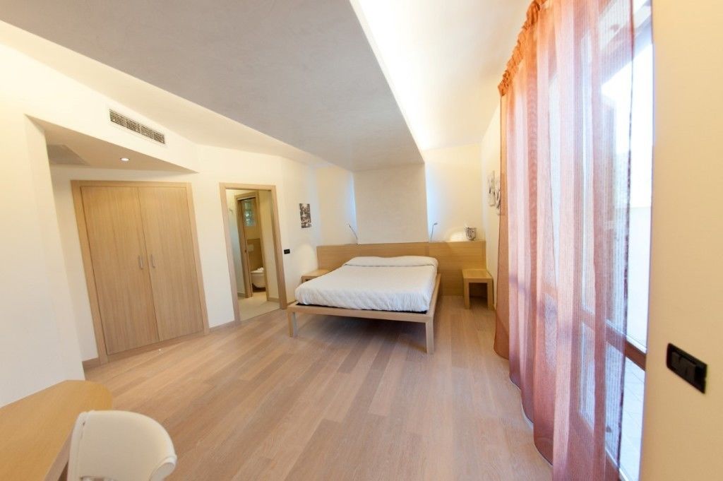 A bedroom with a bed, a wooden wardrobe, a bedside table, and a window with curtains.