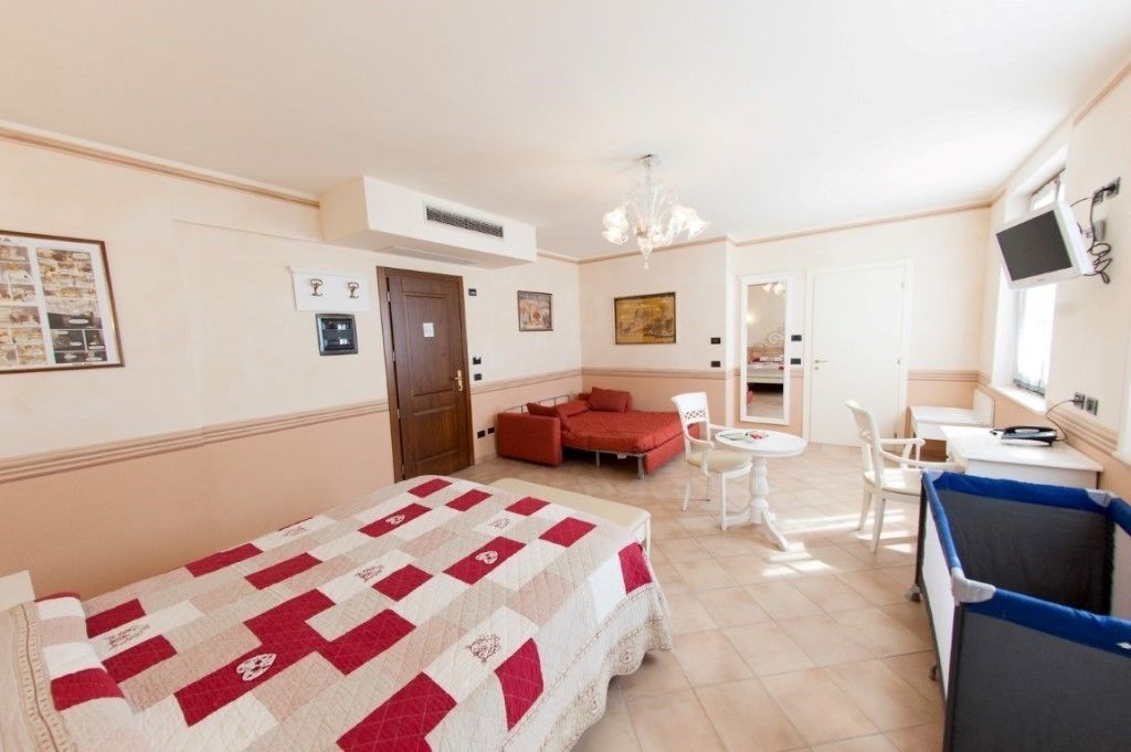 A hotel room with a bed, a red sofa, a small dining table, and a TV.