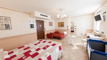 A hotel room with a bed, a red sofa, a small dining table, and a TV.