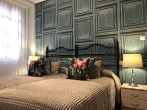 A neatly made bed with floral pillows, a bedside lamp, and a wall with paneling.