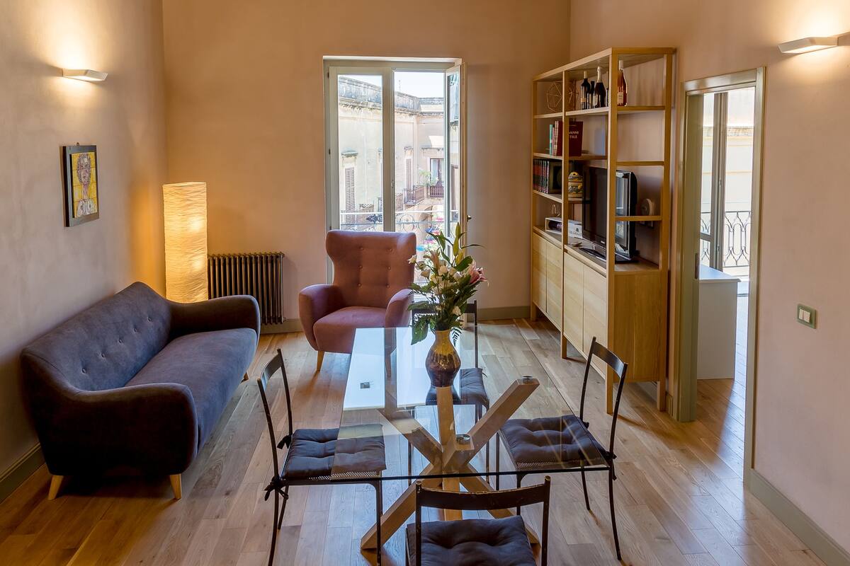 A living room with a sofa, armchair, glass coffee table, and a bookshelf.