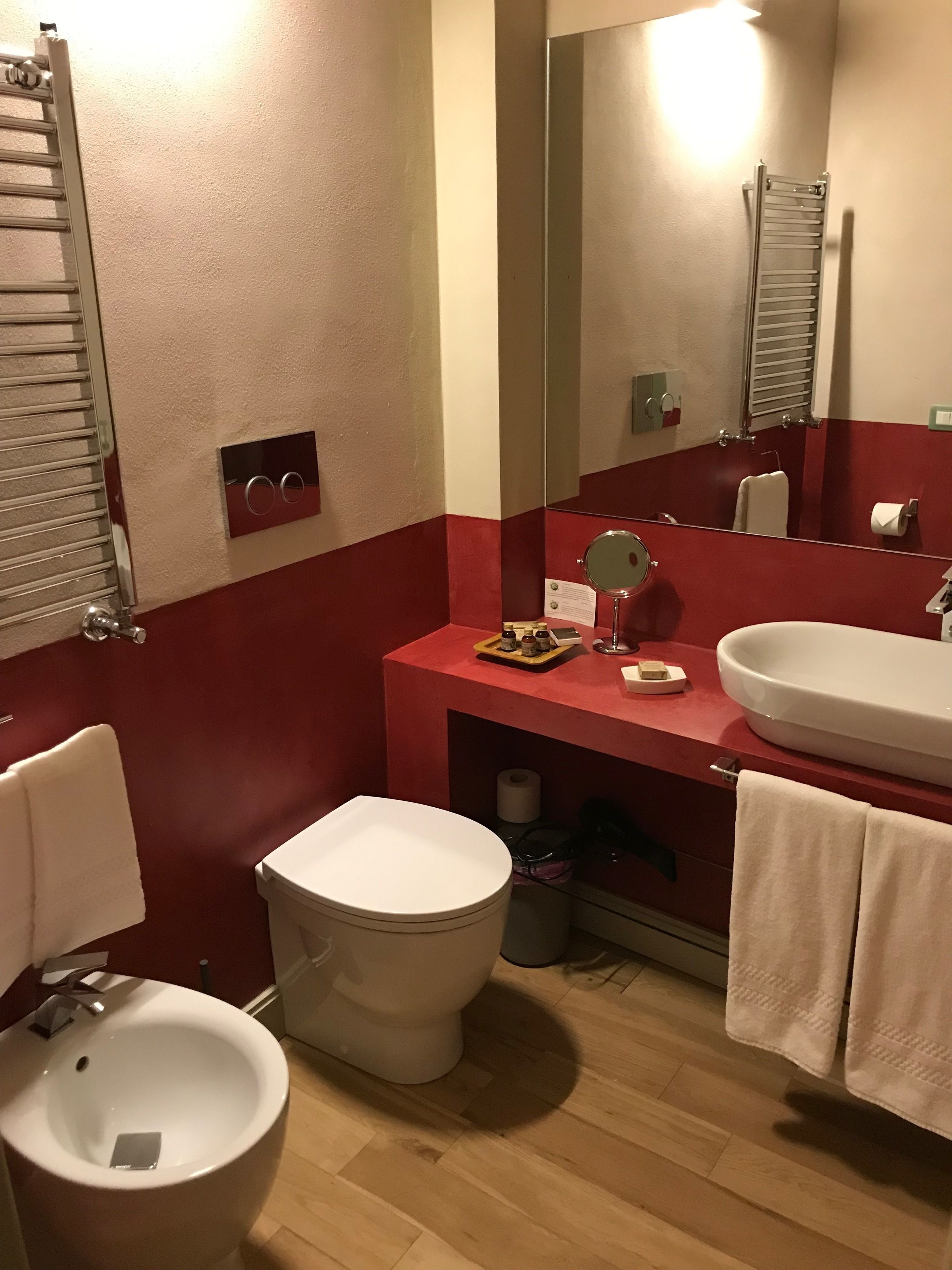 A bathroom with a toilet, sink, mirror, towel rack, and a red accent wall.