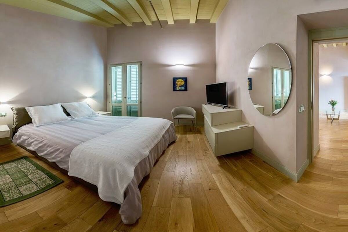 A bedroom with a bed, bedside table, TV, and a mirror.