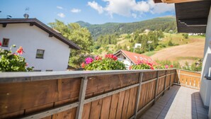 A balcony with a wooden railing overlooking a mountainous landscape with houses and greenery.