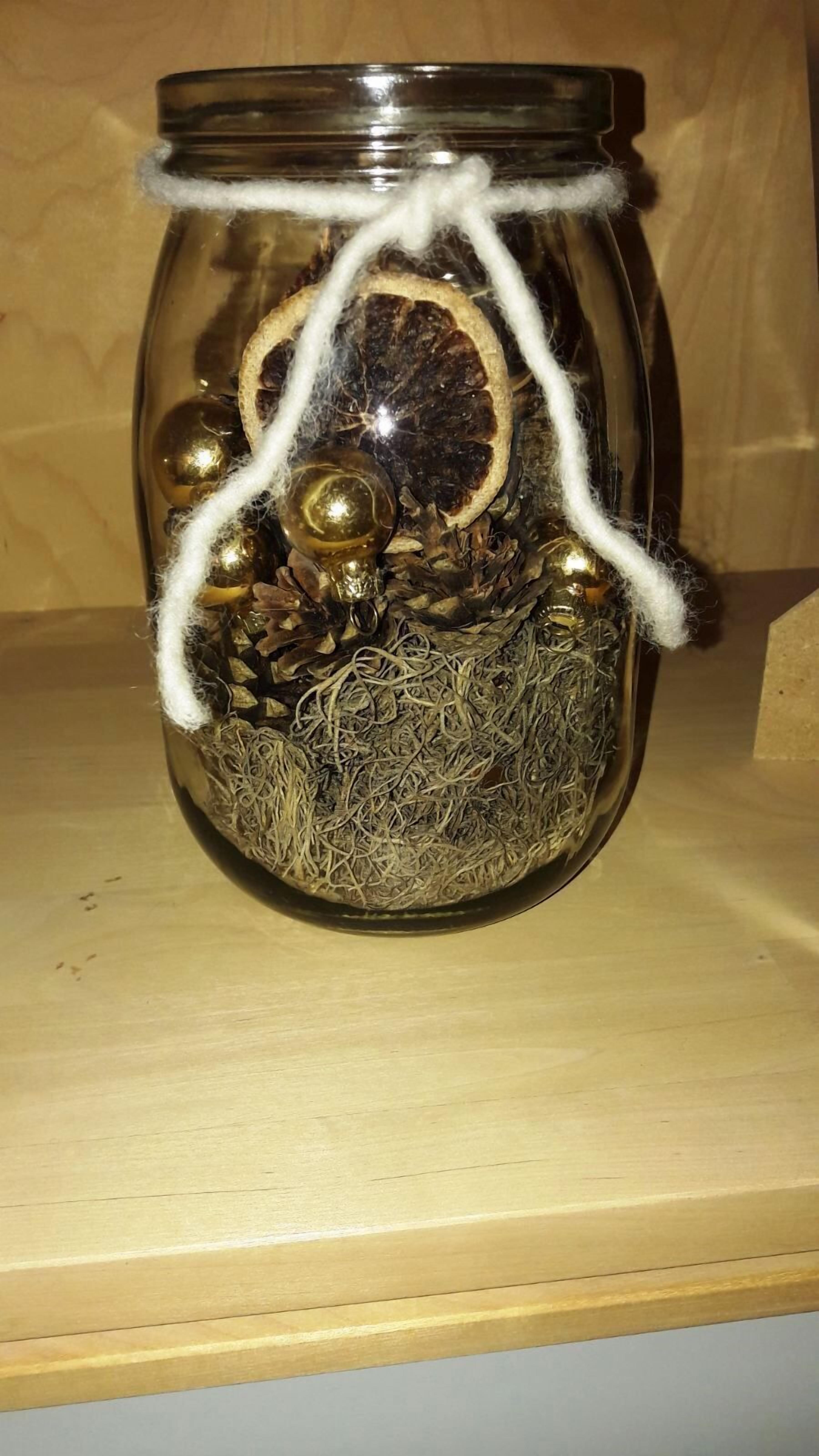 Un bocal en verre entouré d’une ficelle blanche, contenant divers objets, comme une fleur séchée, un petit globe et quelques billes métalliques.