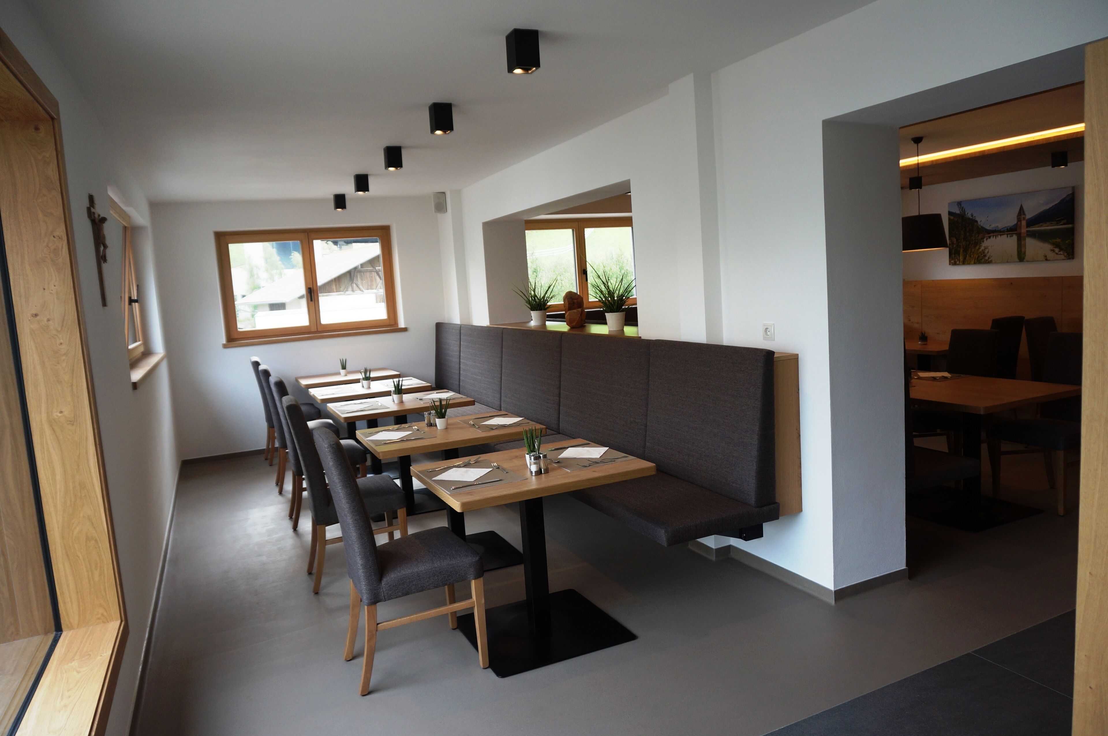 Un restaurante moderno con largas mesas de madera, bancos acolchados y plantas en macetas.