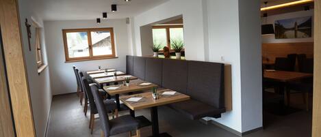 Un restaurante moderno con largas mesas de madera, bancos acolchados y plantas en macetas.
