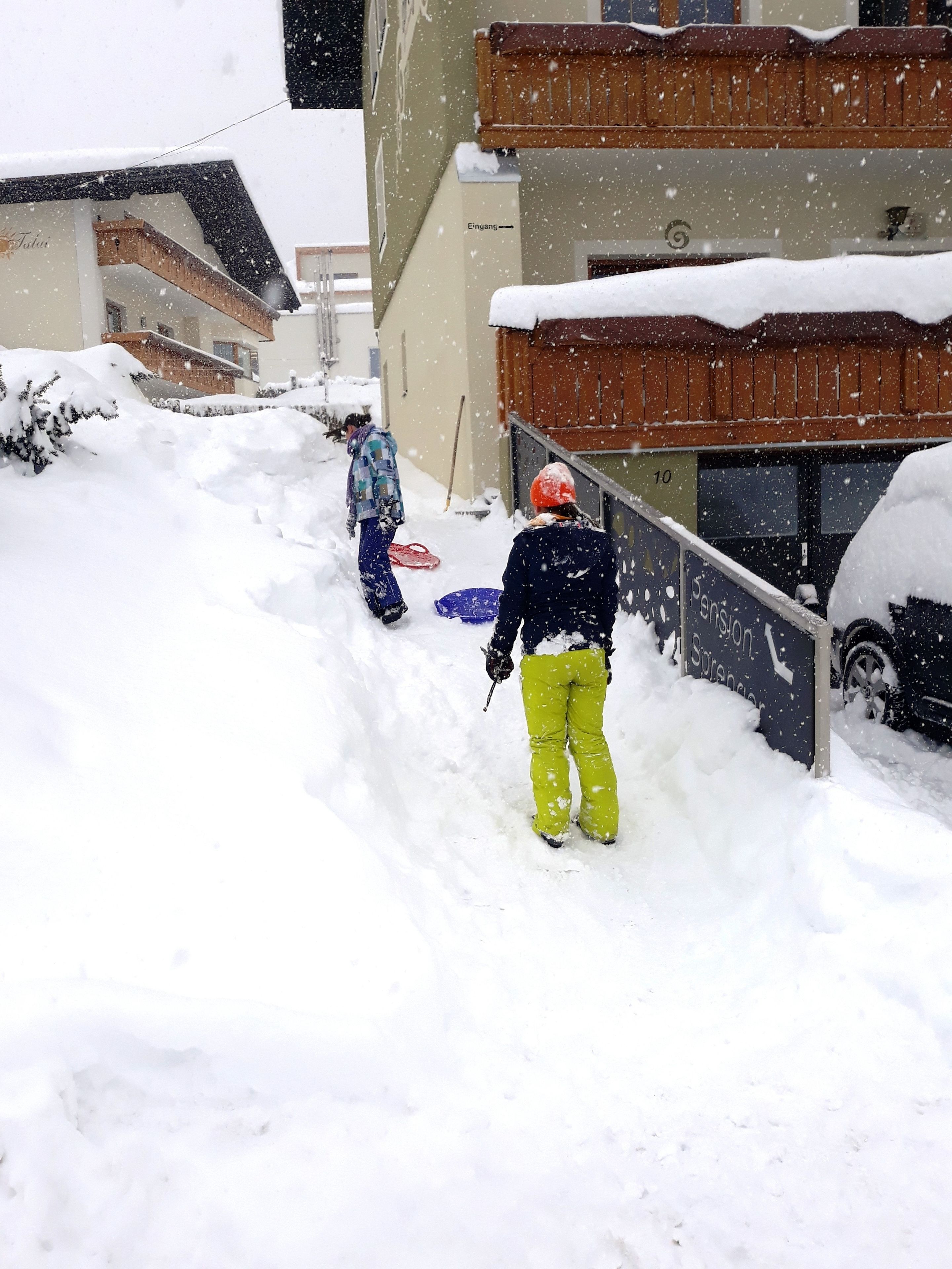 A snowy residential street with houses and a parked car.
