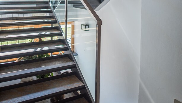 A modern staircase with glass railings and metal supports, leading to an upper floor.