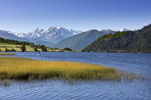 A lake with a boat, surrounded by mountains and grassy areas. - Pension Sprenger (Curon Venosta)