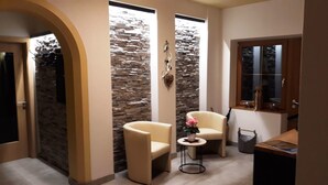 A room with a stone wall, two chairs, a small table with a vase, and a window with blinds.
