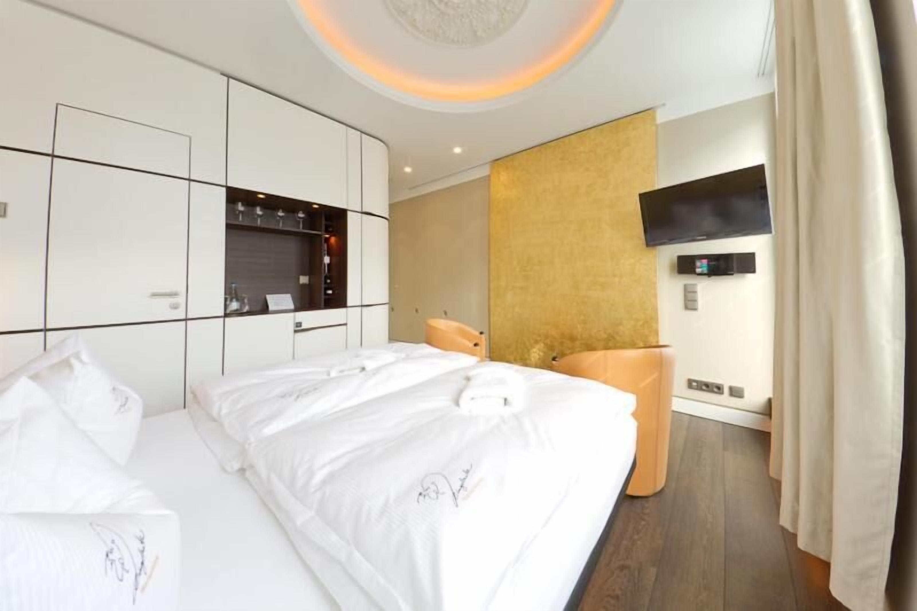 A modern hotel room with a large bed, a TV mounted on the wall, and a minibar.