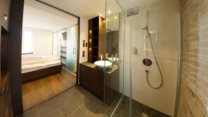 A modern bathroom with a glass-enclosed shower, a vanity with a sink, and a separate bedroom area with a bed. - Ringelnatz Warnemünde (Rostock)
