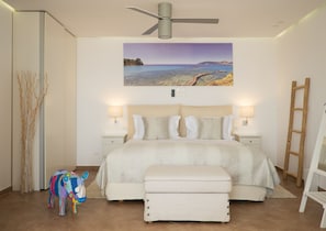 A bedroom with a bed, bedside lamps, a ceiling fan, a painting of a beach, a colorful toy horse, and a wooden ladder. - The Infinity 180 Luxury Suites - Adults Only (Alonissos)