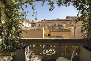 A balcony with a table and chairs, overlooking a cityscape with terracotta-tiled buildings. - Seven Rooms Villadorata (Noto)