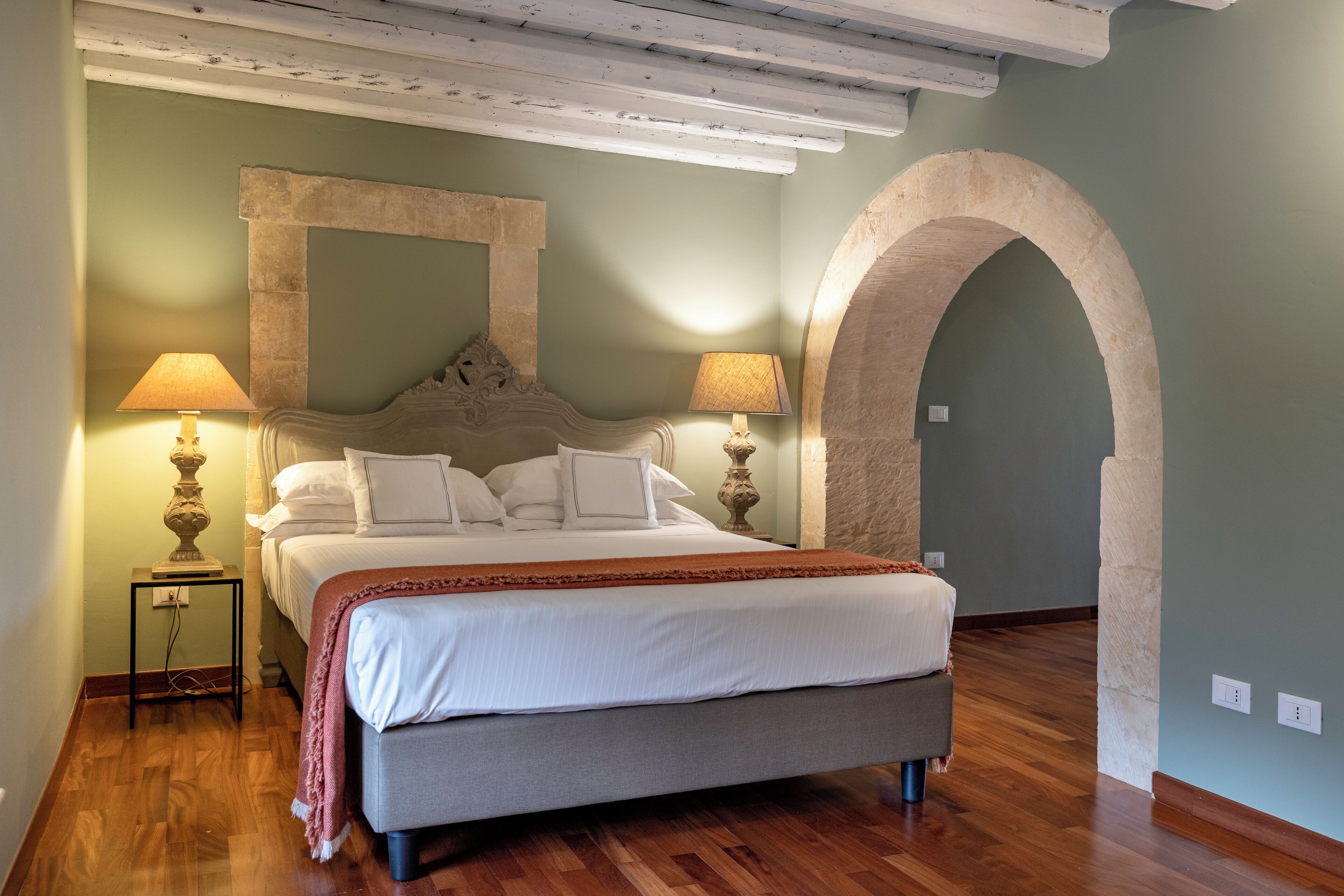 Un dormitorio con una cama, dos lámparas de noche, una mesita de noche y un gran arco de piedra.