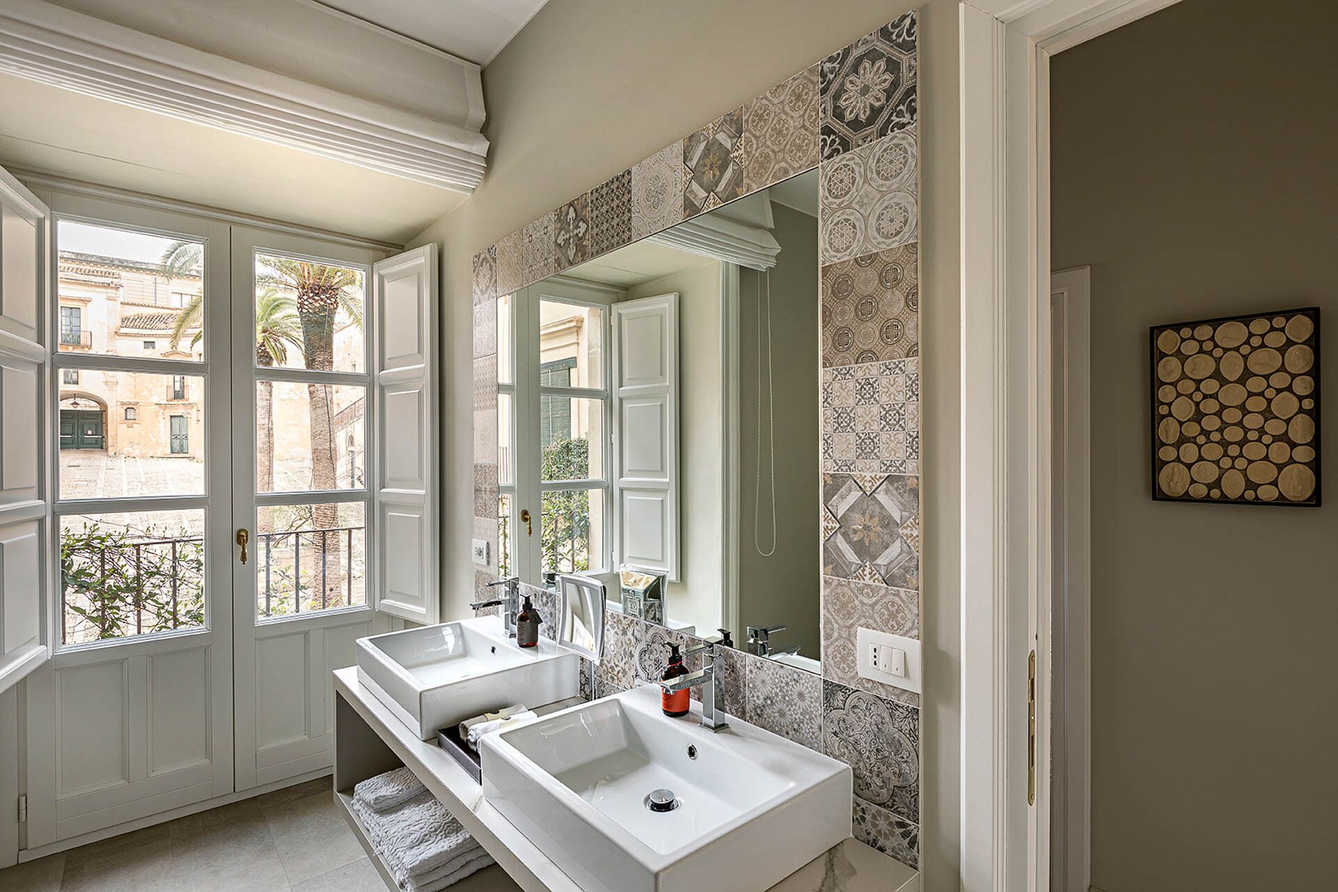 Casa de banho com duas pias, um espelho grande e azulejos estampados.