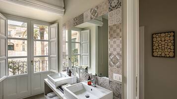 Casa de banho com duas pias, um espelho grande e azulejos estampados.