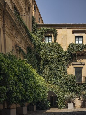 A building with a courtyard, featuring a covered entrance, a small garden area with potted plants, and a staircase leading to an upper level. - Seven Rooms Villadorata (Noto)