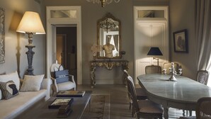 A classic interior with a chandelier, a dining table with chairs, a sofa with cushions, and a mirror with a decorative frame.