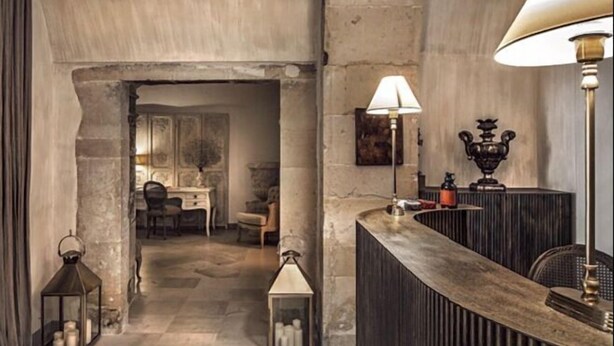 A stone-walled interior with a reception desk, two wall-mounted lamps, and a small table with a lamp.
