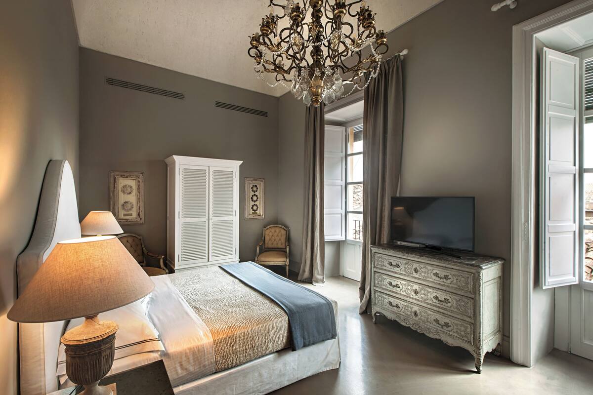 Een slaapkamer met een bed, een kaptafel, een televisie en een kroonluchter.