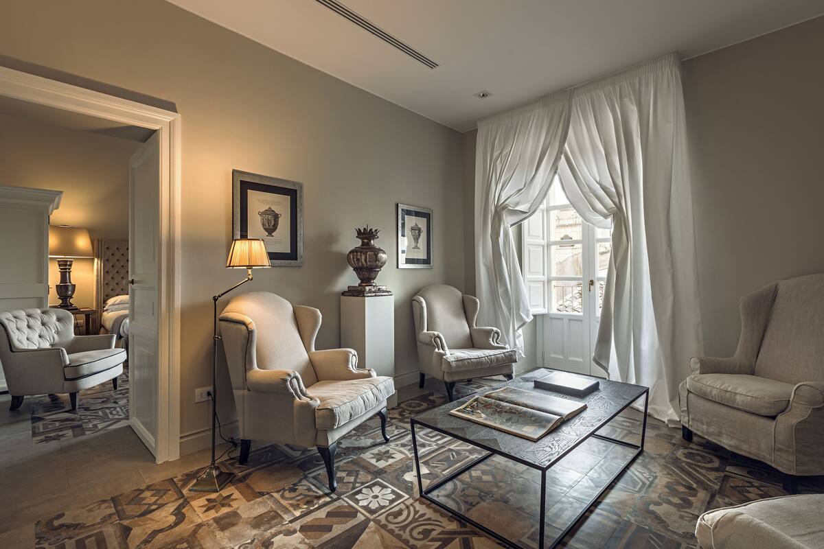 Een ruime woonkamer met een vloer met patroon, een salontafel en drie fauteuils.