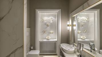 A modern bathroom with a marble floor, a white toilet, a sink with a large mirror, and a display of decorative items in the shower area.