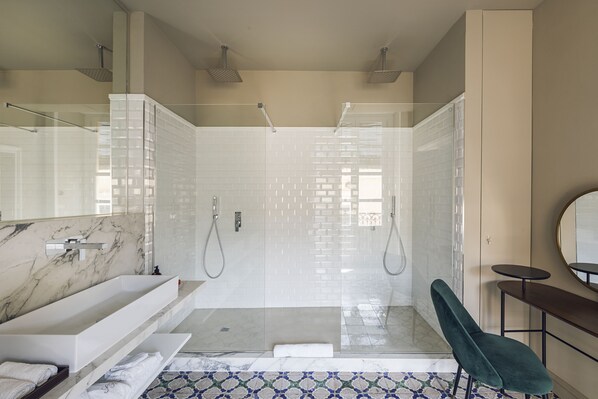 Un baño moderno con un lavamanos de mármol, una ducha con mampara de vidrio y una silla verde.