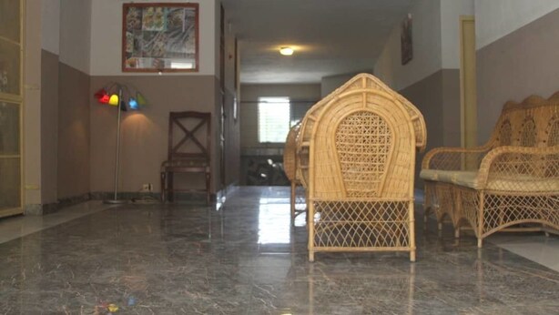 A hallway with a polished marble floor, wicker furniture, and a painting on the wall. - Villa Rosa Hotel & Restaurant (Port-au-Prince)